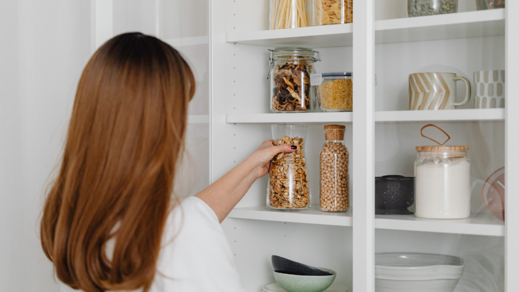 Mulher organizando armário da cozinha com potes e mantimentos.