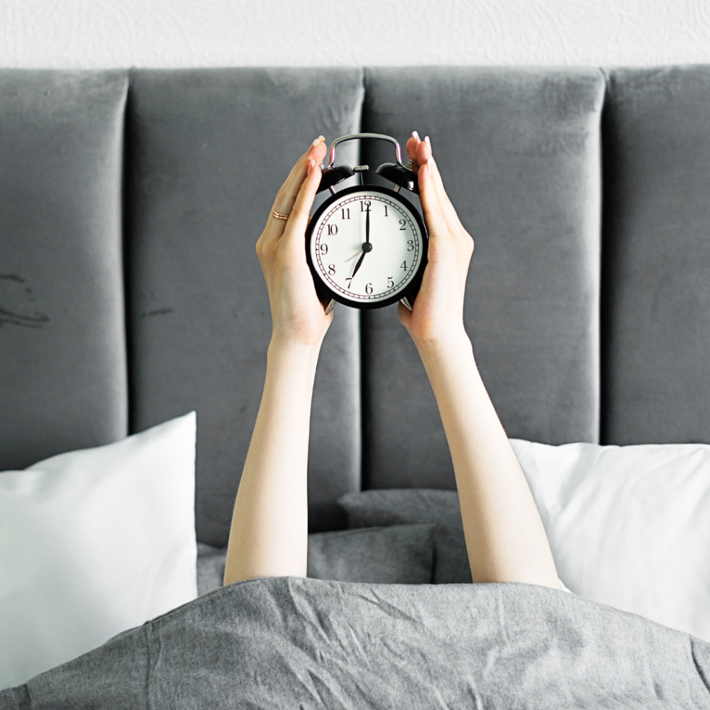 Pessoa deitada na cama segurando um relógio, representando o tempo de sono