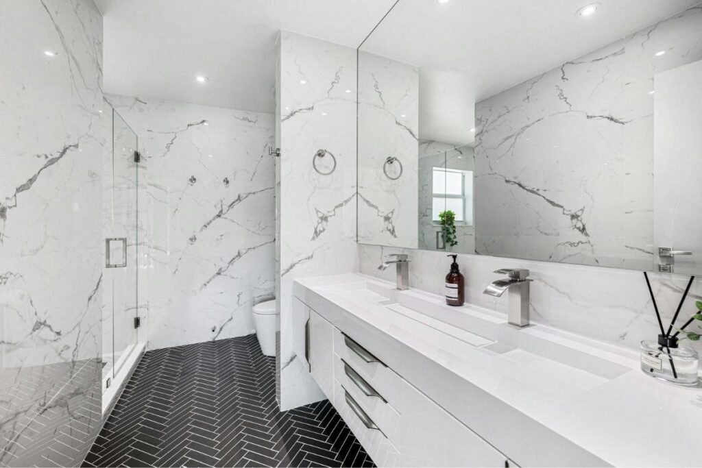 Banheiro moderno neutro com revestimento marmorizado branco, bancada minimalista e box de vidro