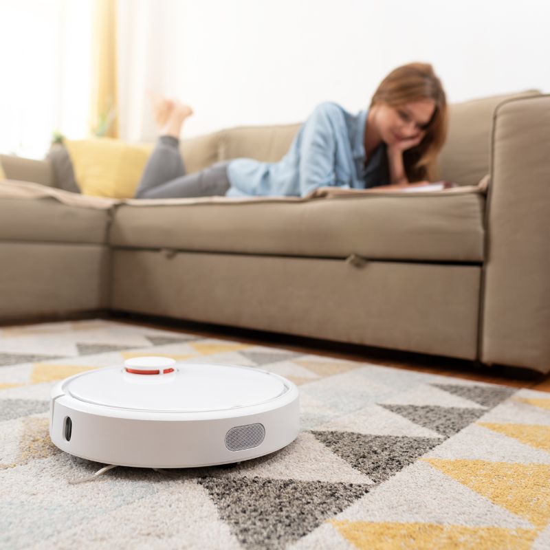 Robô aspirador limpando a sala enquanto mulher relaxa no sofá em casa