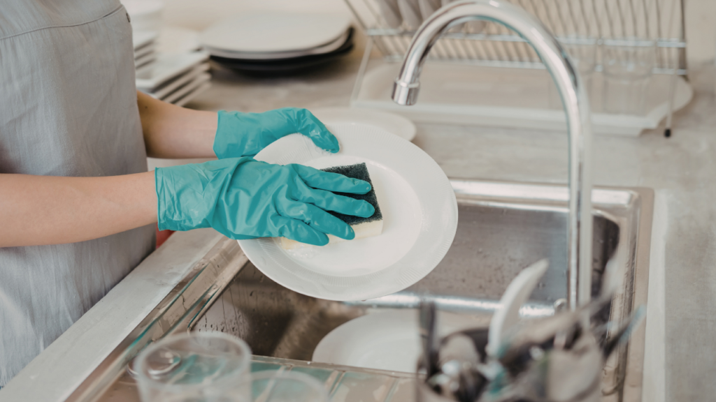 Pessoa lavando um prato com esponja na pia da cozinha para manter a louça e o escorredor sempre limpos.